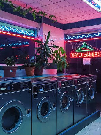 Dry cleaners with a large neon sign and silver washing machines.
