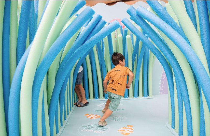 A child running through a maze display full of blue and green pool noodles.