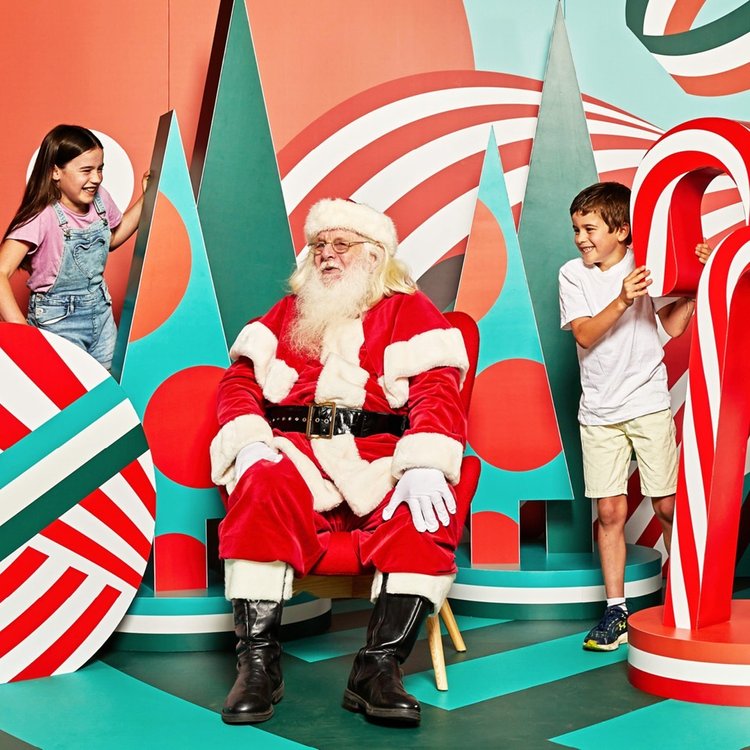 Two children playing on either side of Santa Claus.